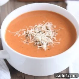 Velvety Instant Pot Tomato Basil Delight 7 White bowl with handles filled with creamy tomato basil soup with Parmesan for topping
