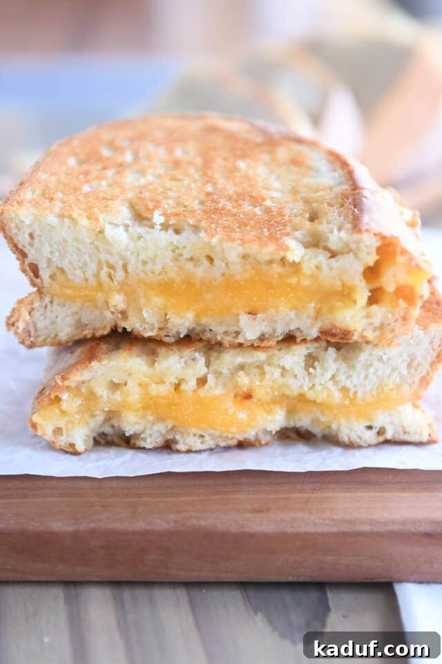 Effortless Rustic Sourdough Loaf 3 Two half slices of a perfectly golden grilled cheese sandwich made with sourdough peasant bread on a rustic wood cutting board.