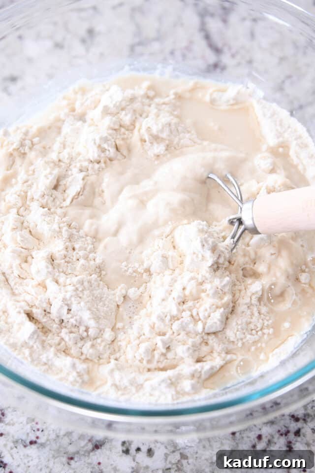 Effortless Rustic Sourdough Loaf 5 Mixing wet sourdough bread dough with a Danish dough whisk in a glass bowl, showcasing the shaggy texture.