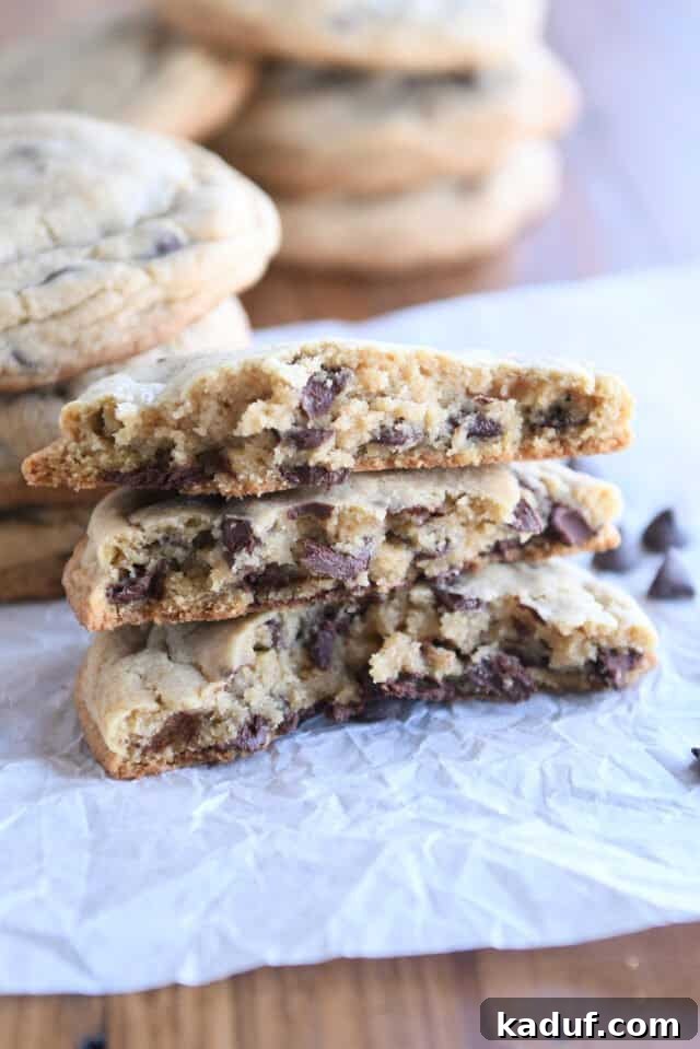 Velvety Oat Chocolate Chip Cookies 6 Three half cookies stacked on white parchment paper, showing soft, chocolatey interiors.