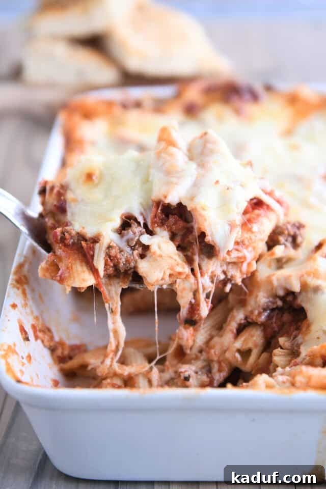Your Go-To Cheesy Meal Prep Pasta Bake 2 Scooping a hearty serving of cheesy weeknight pasta bake from a white 9X13-inch baking dish, ready to be enjoyed by the family.