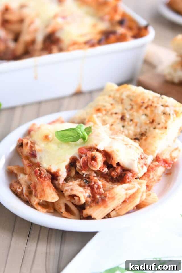 Your Go-To Cheesy Meal Prep Pasta Bake 6 A generous serving of cheesy pasta bake on a white plate, accompanied by a slice of focaccia bread, promising a complete and satisfying meal.