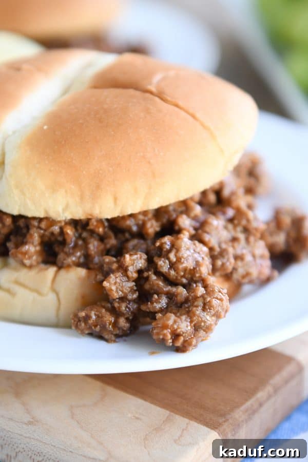 Seriously Delicious Sloppy Joes 3 Close-up of sloppy joe meat generously spilling over a toasted bun onto a white plate, highlighting its rich texture.