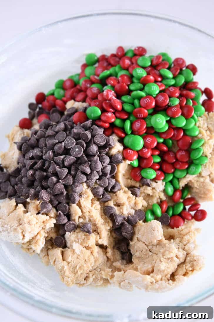 Festive M&M Holiday Cookies 4 Image of a glass bowl with cookie batter, chocolate chips, and red and green M&Ms mixed in.