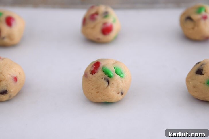 Festive M&M Holiday Cookies 5 Image of a sheet pan with cookie dough balls on parchment paper ready to be baked.