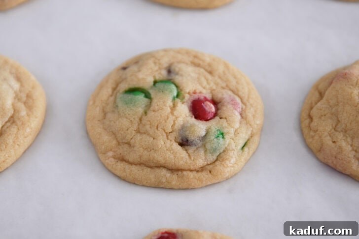 Festive M&M Holiday Cookies 6 Image of baked M&M Christmas cookies on parchment paper cooling after baking.