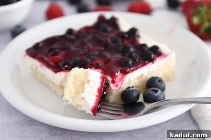 Grandma's Secret Sheet Cake Recipe 10 A square of Grandma's Famous Sheet Cake with cream cheese layer and fruit topping on a white plate with fresh blueberries.