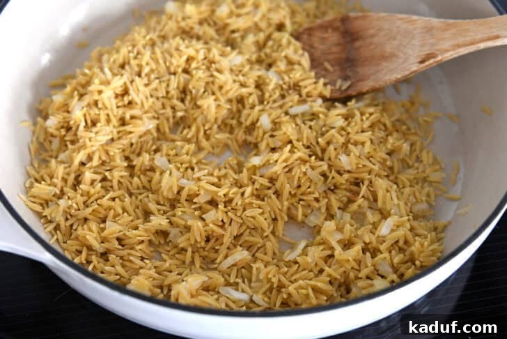 Zesty One-Pot Creamy Chicken Orzo 5 White pan with toasted orzo and onions.