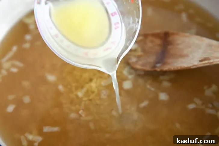 Zesty One-Pot Creamy Chicken Orzo 6 Pouring broth into white pot with onions and orzo.