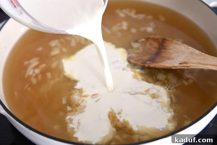 Zesty One-Pot Creamy Chicken Orzo 7 Pouring cream into white pan with broth and orzo.