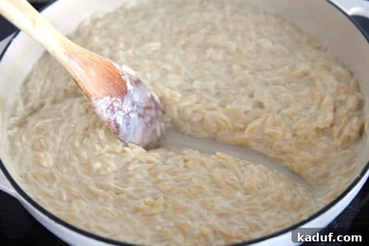 Zesty One-Pot Creamy Chicken Orzo 8 Wooden spoon scraping path through creamy orzo in white pan.