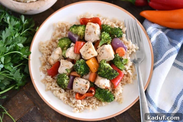 Sweet & Sticky Sheet Pan Chicken Dinner 3 White plate with tan rim with brown rice, cooked chicken, broccoli, red onions, bell peppers, carrots and red onions.