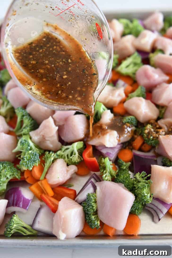 Sweet & Sticky Sheet Pan Chicken Dinner 5 Pouring honey garlic sauce over chicken, broccoli, bell peppers, and carrots on sheet pan.