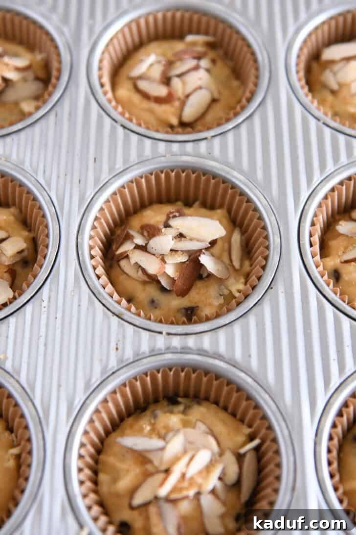 Decadent Almond Coconut Chocolate Chip Muffins 6 Unbaked almond coconut chocolate chip muffin batter in muffin tins topped with sliced almonds.