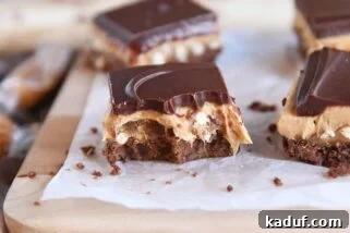 peanut butter pretzel caramel chocolate bar on piece of white parchment paper with bite taken out