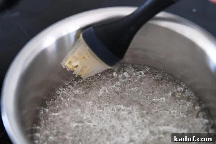 Pastry brush brushing down sides of saucepan with simmering sugar and water.