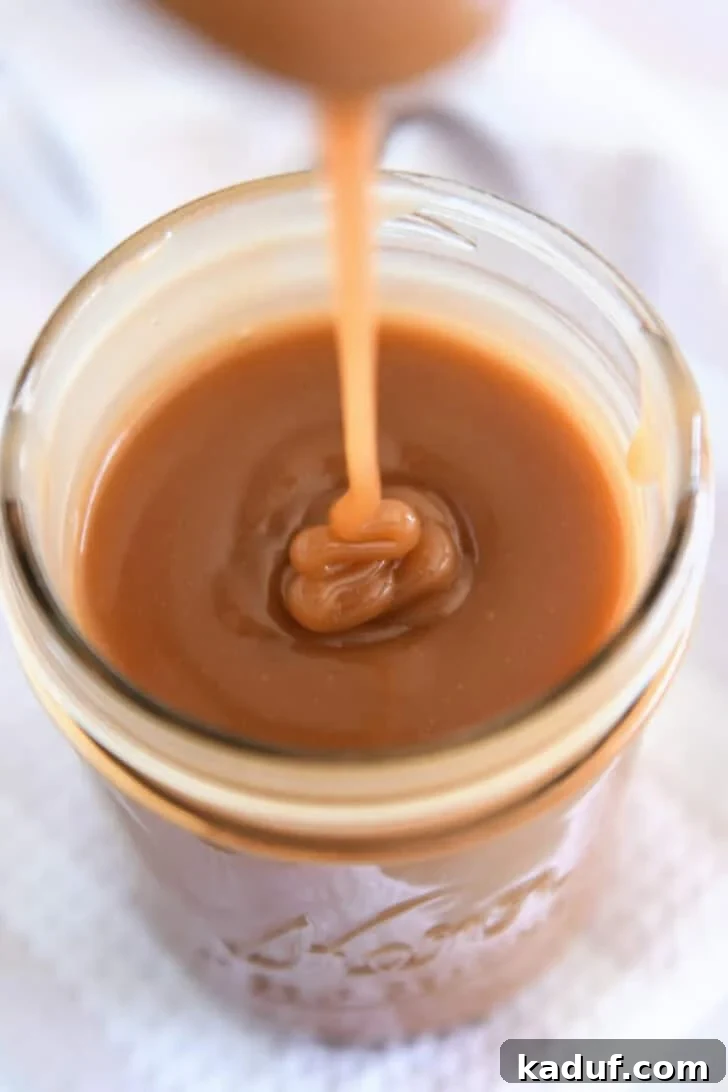 Drizzling caramel sauce from spoon into glass jar.