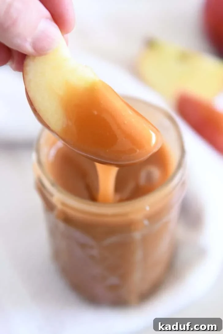 Dipping apple slice into jar of caramel sauce.