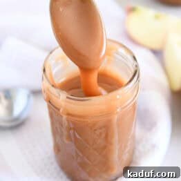 Spoon drizzling caramel sauce into glass jar with apple in the background.