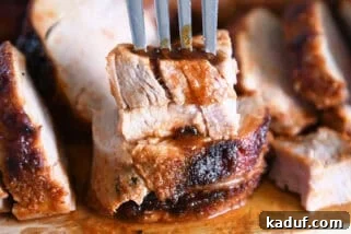 Fork piercing two stacked pieces of cooked pork tenderloin on wood cutting board.