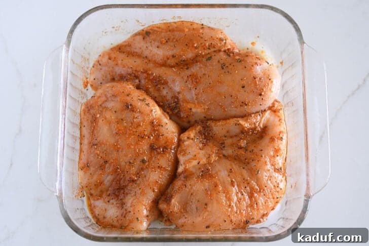 Three seasoned, uncooked chicken breasts in glass square pan.