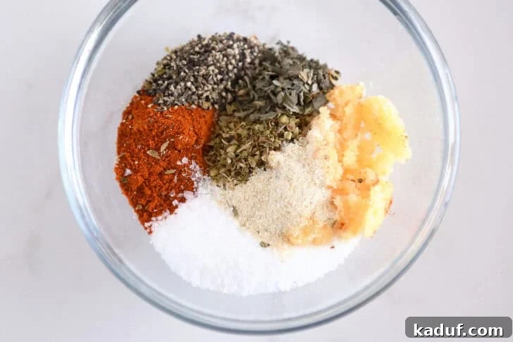 Salt, onion powder, fresh garlic, oregano, basil, pepper and smoked paprika in glass bowl.