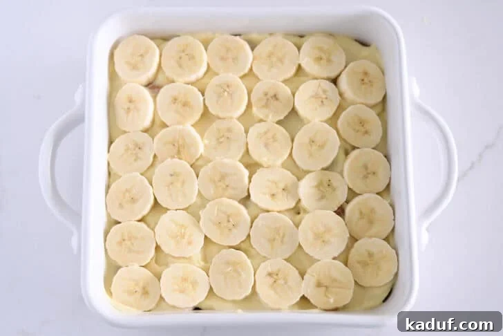 Homemade Banana Pudding from Scratch: Creamy Classic Recipe 11 White square 8X8 baking dish with sliced bananas over the vanilla pudding.