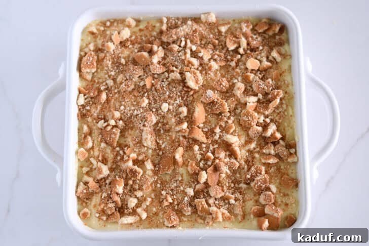 Homemade Banana Pudding from Scratch: Creamy Classic Recipe 13 Crumbled Nilla wafers on top of vanilla pudding in white 8X8 pan.