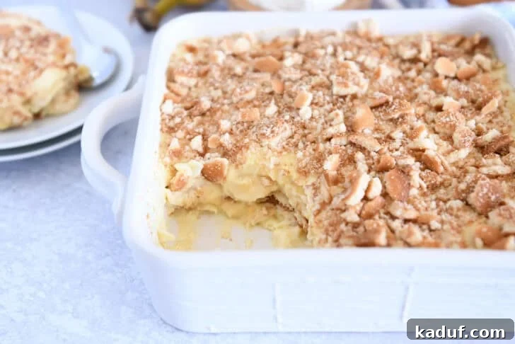 Homemade Banana Pudding from Scratch: Creamy Classic Recipe 3 Crumbled Nilla wafers on top of vanilla pudding in white 8X8 pan with scoop taken out of corner.