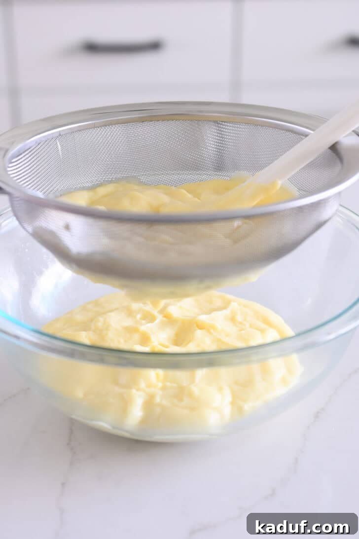 Homemade Banana Pudding from Scratch: Creamy Classic Recipe 7 Straining vanilla pudding through fine mesh strainer into glass bowl.