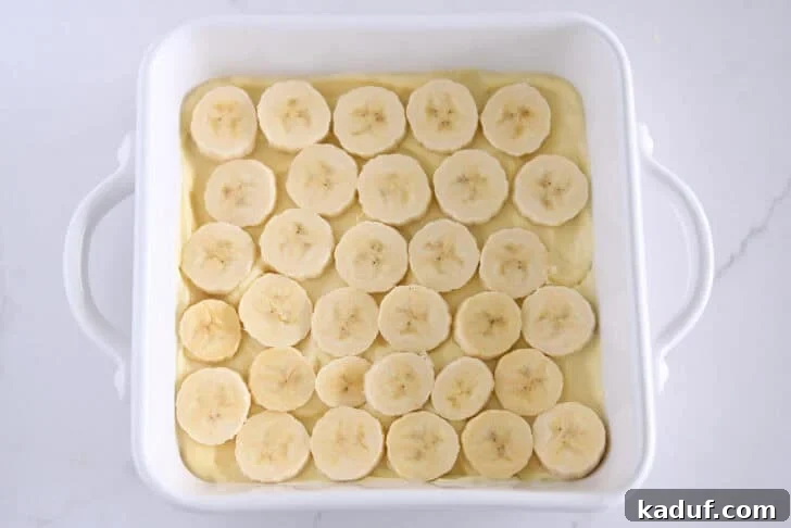 Homemade Banana Pudding from Scratch: Creamy Classic Recipe 8 White square 8X8 baking dish with layer of vanilla pudding and sliced bananas.