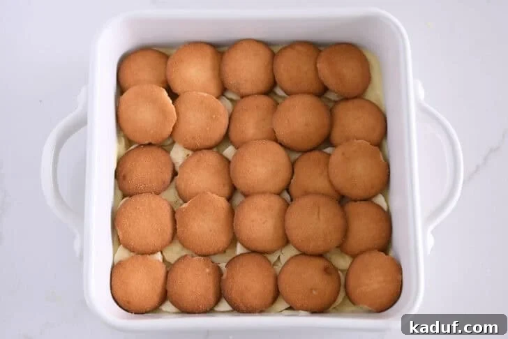 Homemade Banana Pudding from Scratch: Creamy Classic Recipe 9 White square 8X8 baking dish with layer of vanilla pudding, sliced bananas, and nilla wafers.