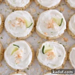 Lots of frosted coconut lime sugar cookies topped with toasted coconut and a fresh lime wedge on white parchment paper.