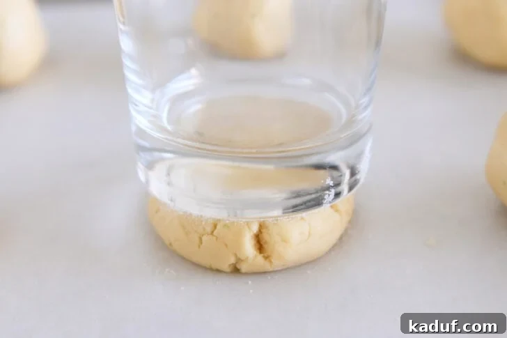 Pressing sugar cookie dough ball into thick disc with sugared bottom drinking glass.