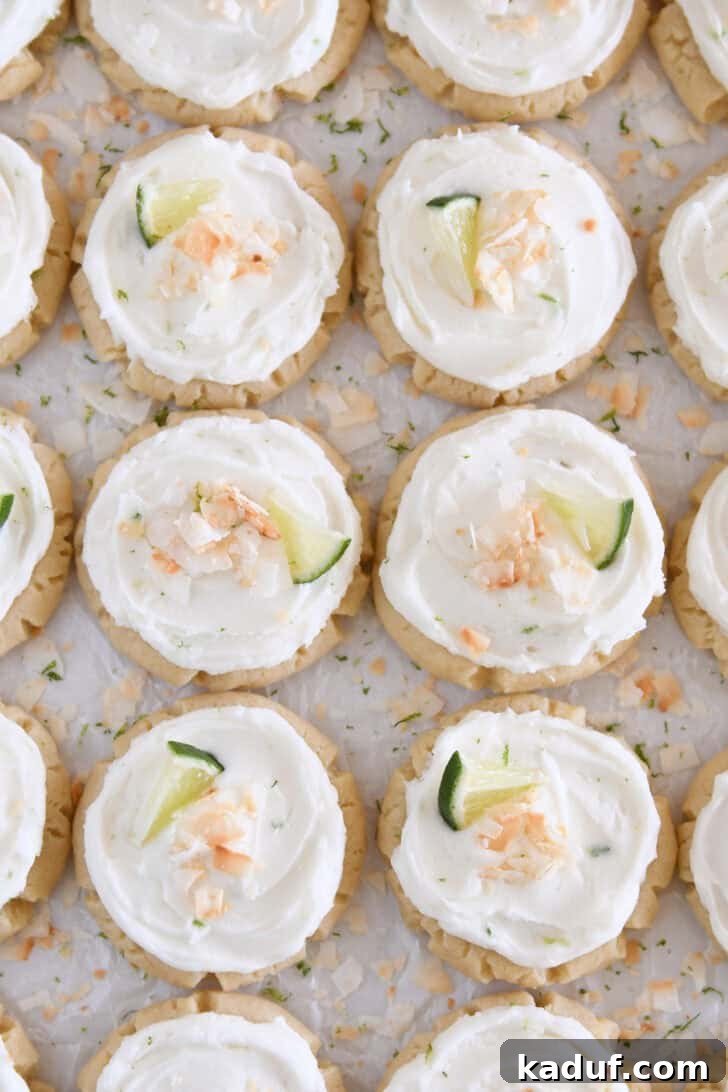 Lots of frosted coconut lime sugar cookies topped with toasted coconut and a fresh lime wedge on white parchment paper.