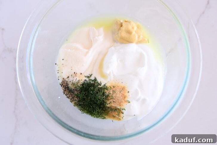 Tangy Dill Pickle Chicken Salad Recipe 5 Glass bowl with mayo, greek yogurt, dijon mustard, dill, onion powder, black pepper and garlic powder.