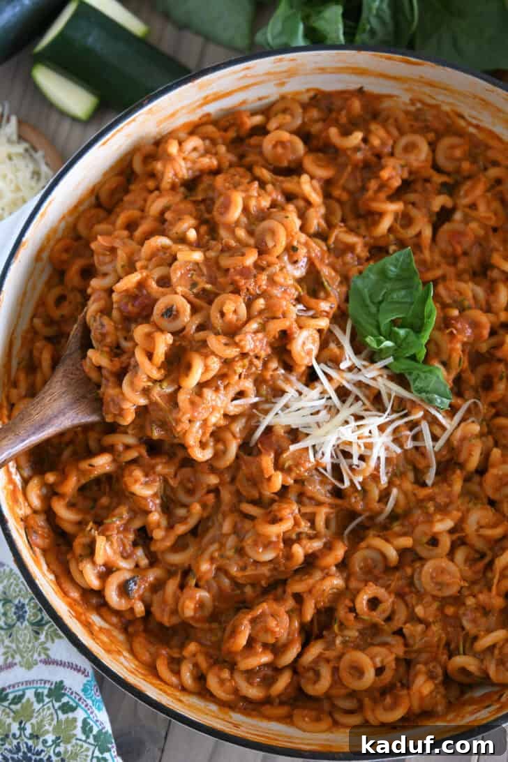 One-Pot Saucy Zucchini Pasta for Quick Weeknight Meals 2 Serving spoon scooping up helping of saucy pasta out of deep skillet.