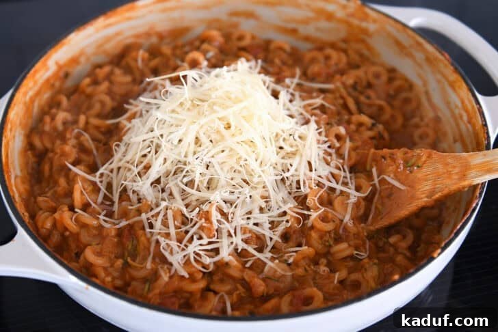 One-Pot Saucy Zucchini Pasta for Quick Weeknight Meals 6 Adding freshly grated Parmesan to cooked pasta in red sauce with shredded zucchini in deep skillet.