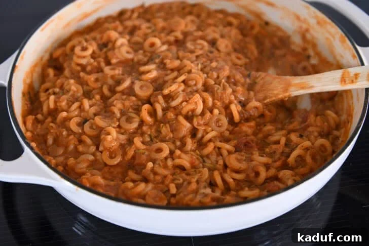 One-Pot Saucy Zucchini Pasta for Quick Weeknight Meals 7 Cooking pasta in red sauce with shredded zucchini in deep skillet.