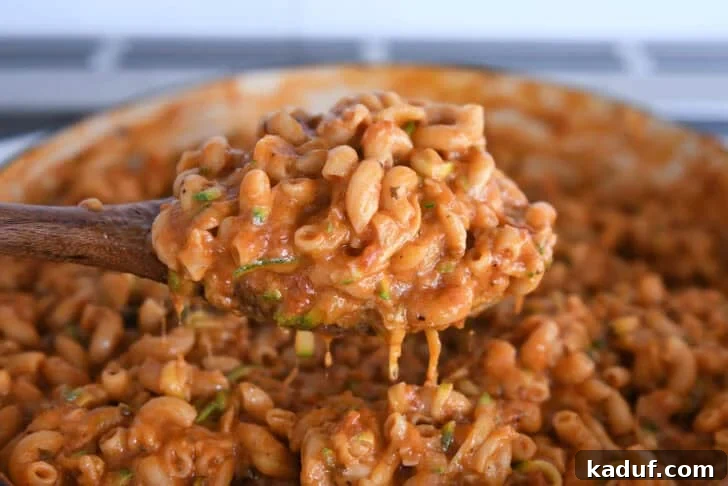 One-Pot Saucy Zucchini Pasta for Quick Weeknight Meals 8 Spoon scooping up serving of saucy pasta with shredded zucchini in skillet.