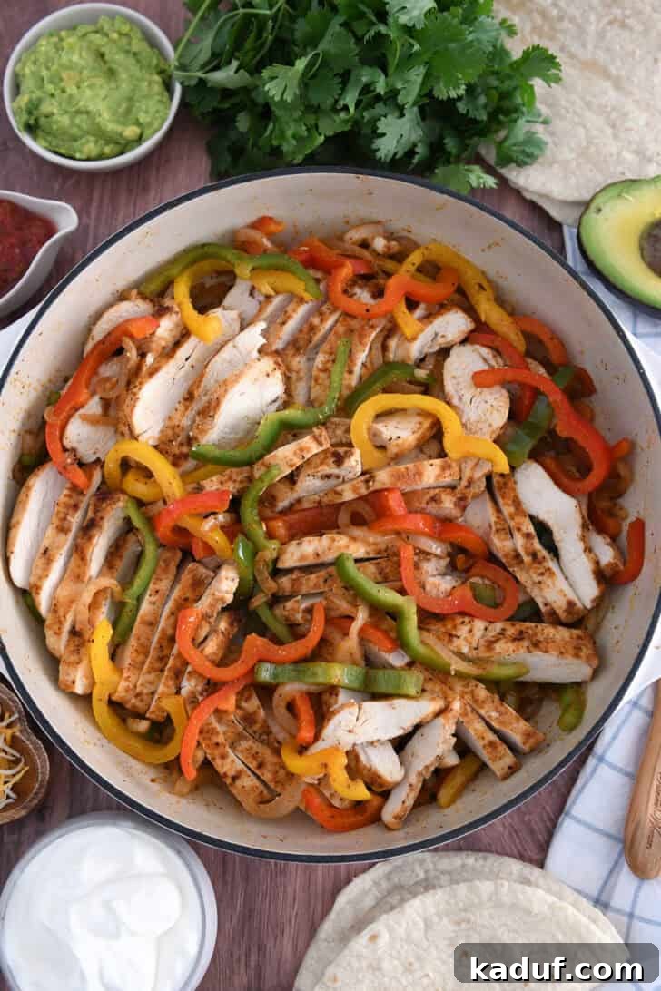 Weeknight Chicken Fajitas with Peppers and Onions 2 Top down view of white cast iron skillet filled with sliced fajita chicken breasts, bell peppers and onions.