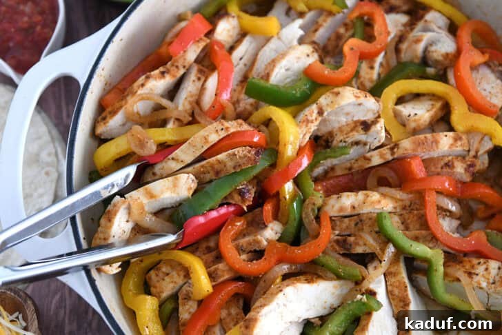 Weeknight Chicken Fajitas with Peppers and Onions 7 White cast iron skillet filled with sliced fajita chicken breasts, bell peppers and onions.