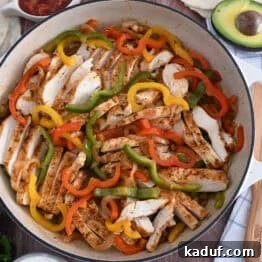 Top down view of white cast iron skillet filled with sliced fajita chicken breasts, bell peppers and onions.